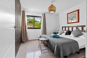 A bedroom with a bed, curtains, a window with a view, a bedside lamp, and a wall-mounted artwork.
