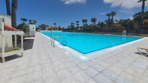A swimming pool with a tiled deck, surrounded by palm trees and buildings. - Holiday Home 'Apartamento Papagayo' with Shared Pool, Private Terrace & Wi-Fi (Corralejo)