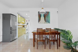 Uma sala de jantar com mesa e cadeiras de madeira, uma geladeira, uma máquina de lavar e um grande quadro abstrato na parede.