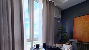 A modern living room with a round table, two armchairs, a large window with curtains, a potted plant, and a wall-mounted artwork. - ELUDE Designer Suite Pasig (Prime location) (pasig city)