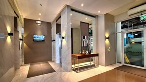 A modern lobby with a marble floor, a reception desk, a TV screen, and a glass door leading to a parking area. - ELUDE Designer Suite Pasig (Prime location) (pasig city)