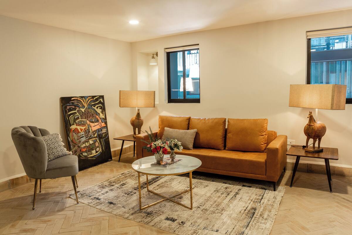 Una sala de estar con sofá, sillón, mesa de centro y dos mesitas de noche con lámparas.