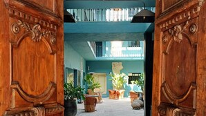 A spacious courtyard with a cobblestone path, wooden doors with intricate carvings, and a view of the upper floor with seating areas and potted plants. - Casa Nduxi (Puebla)