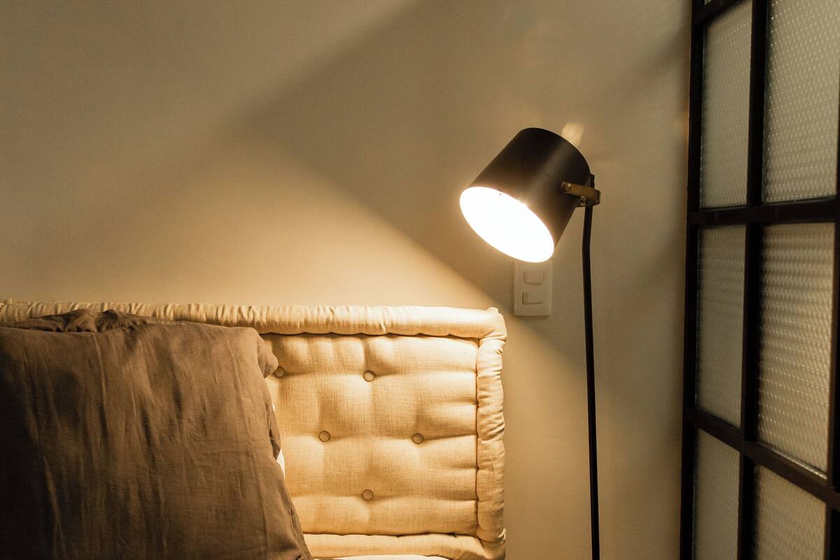 Una cama bien hecha con cabecera, lámpara de noche y mesita de noche.