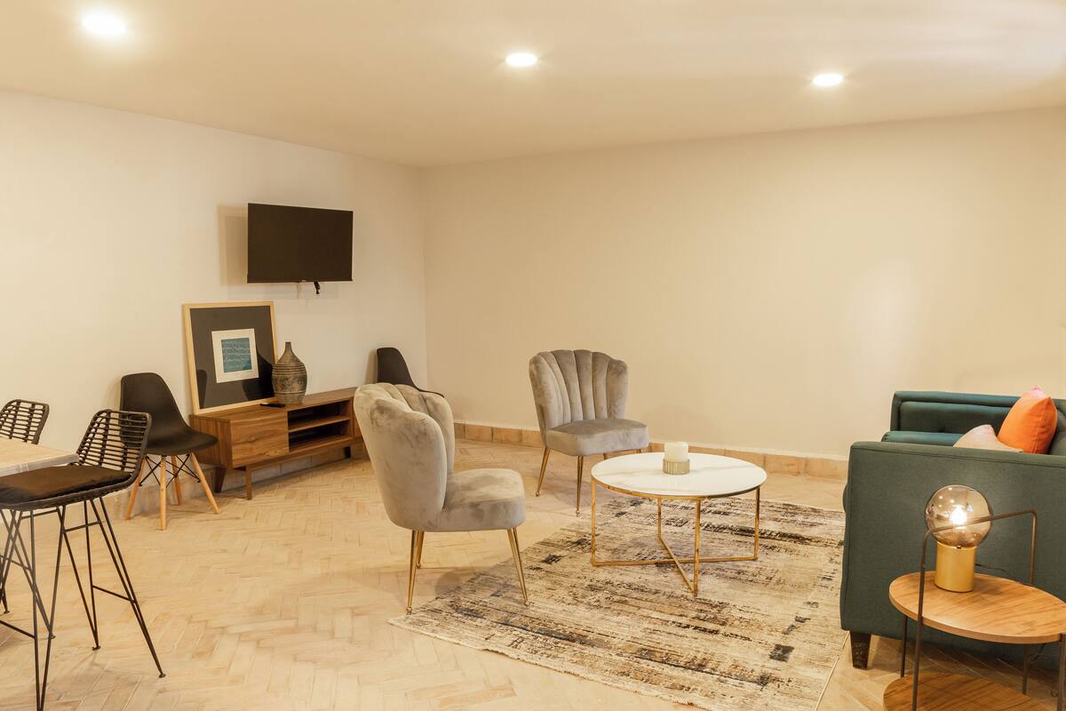 Una sala de estar moderna con un sofá, dos sillones, una mesa de centro y un televisor montado en la pared.