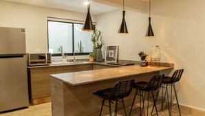 A modern kitchen with a large island, bar stools, pendant lighting, and a refrigerator. - Casa Nduxi (Puebla)