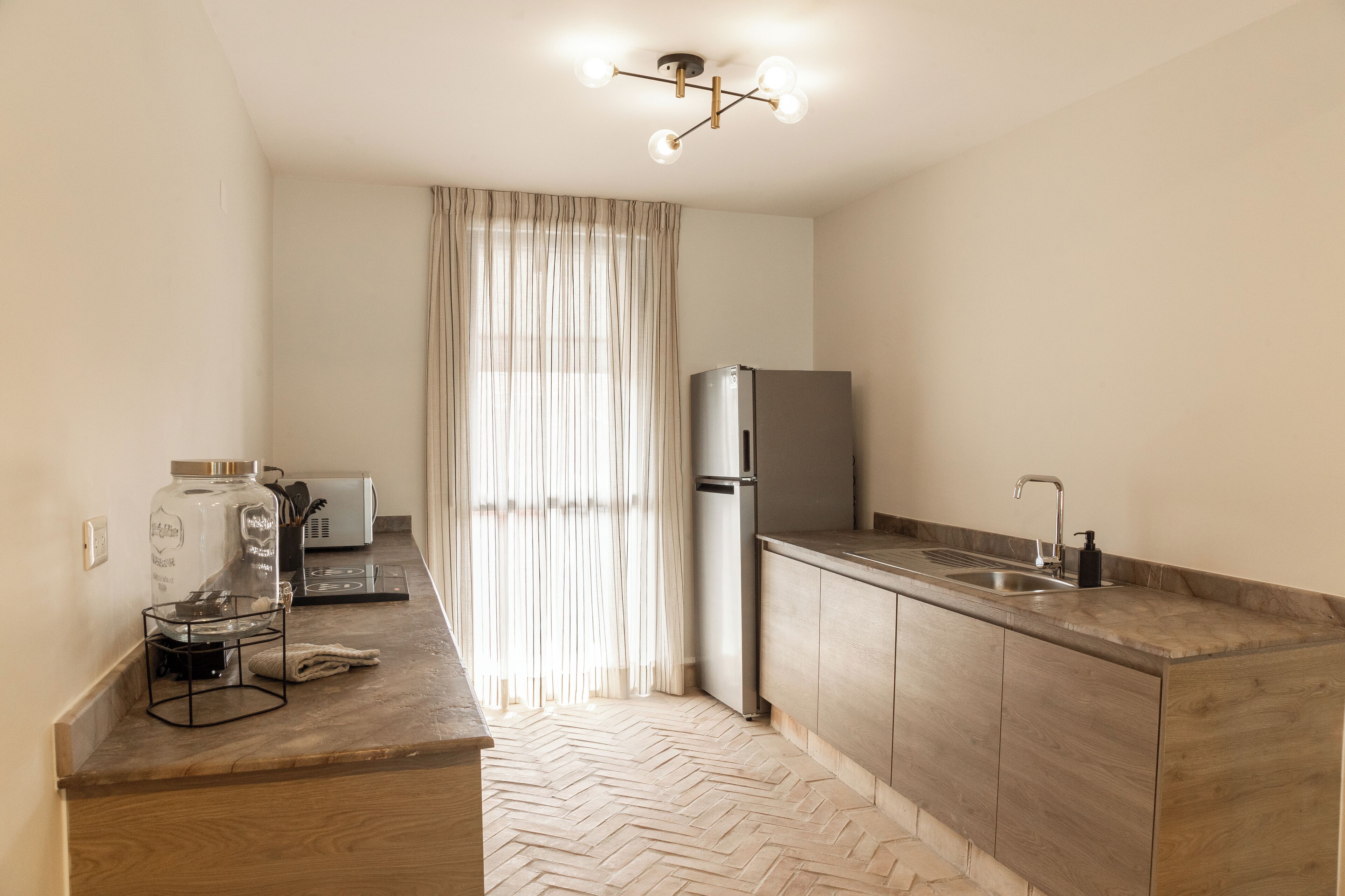 A modern kitchen with a herringbone floor pattern, a stainless steel refrigerator, a built-in sink, and a pendant light fixture.
