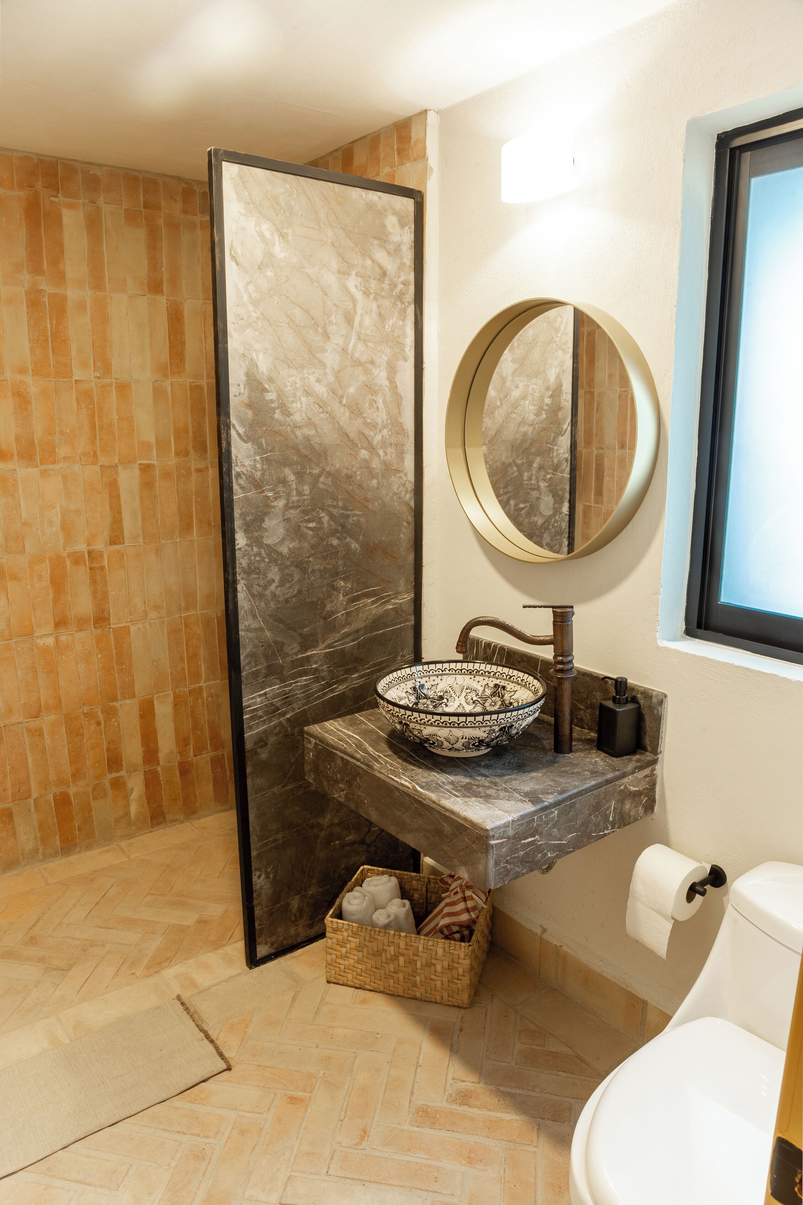 A bathroom with a marble sink, a round mirror, a toilet, and a shower area with a tiled floor.