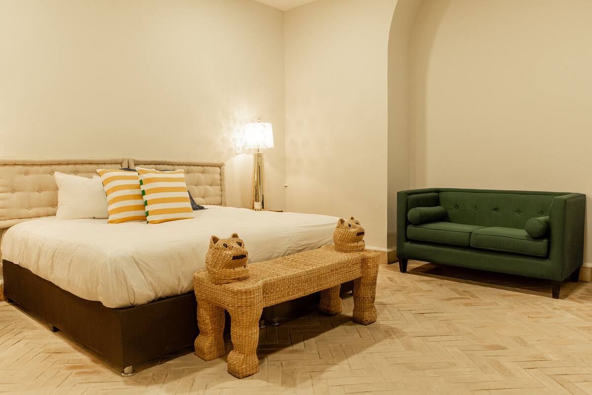 Un dormitorio con una cama, un sofá verde y un banco tejido con figuras de animales.