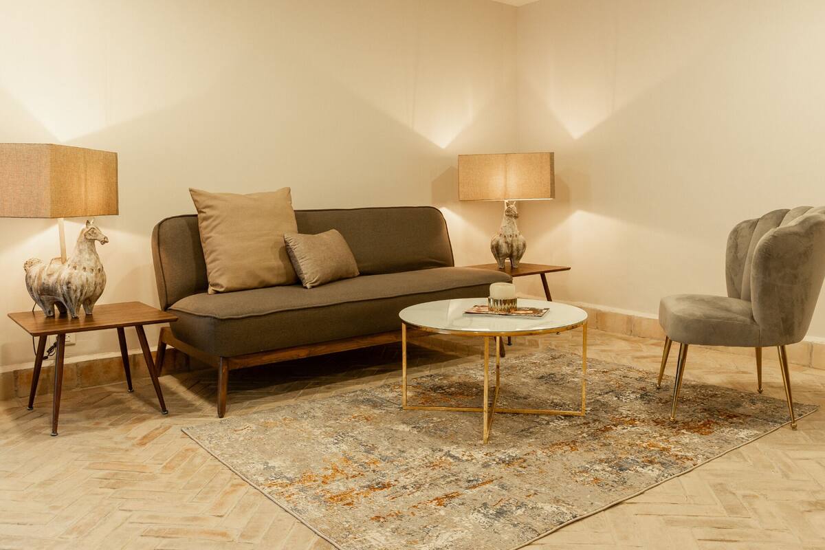 Una sala de estar con un sofá, dos mesas auxiliares, una mesa de centro, una alfombra y una silla.
