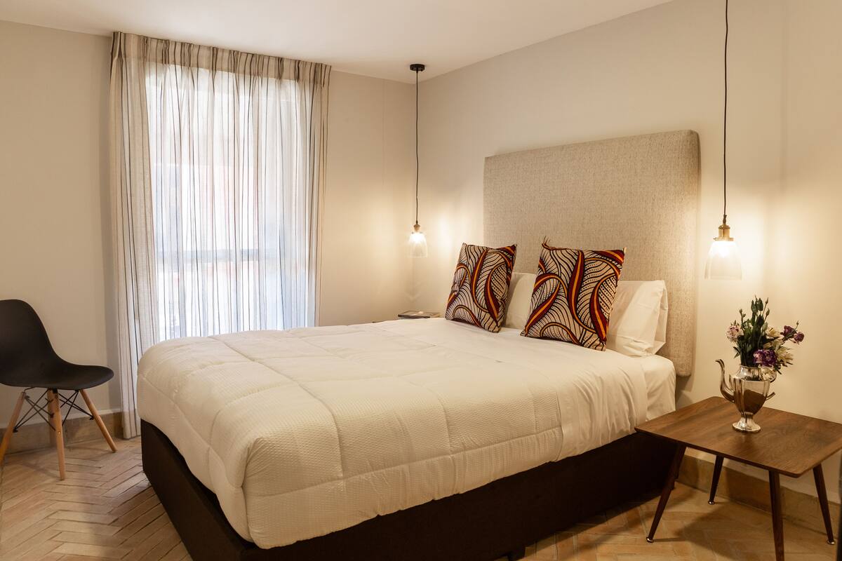 Un dormitorio moderno con una cama grande, una mesita de noche con un florero y una silla.