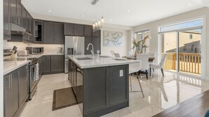 A modern kitchen with dark cabinets, a large island, and a dining area with a view to the outside. - Executive 5BR-4BATH Detached Retreat Brampton/Miss Border  (Brampton)