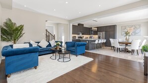 A spacious living area with a blue sofa set, a dining table with white chairs, and a kitchen in the background. - Executive 5BR-4BATH Detached Retreat Brampton/Miss Border  (Brampton)