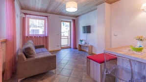 A cozy living room with a sofa, a dining table with chairs, a TV mounted on the wall, and a wooden ceiling. - Villa Edelweiss Botton d'oro (Alleghe)