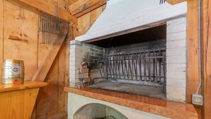 A brick oven with a metal rack inside, a wooden shelf with a can on it, and a brick wall. - Villa Edelweiss Botton d'oro (Alleghe)