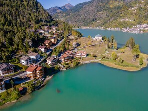 An aerial view of a lakeside village with buildings clustered around the shore, a small island, and mountains in the background.