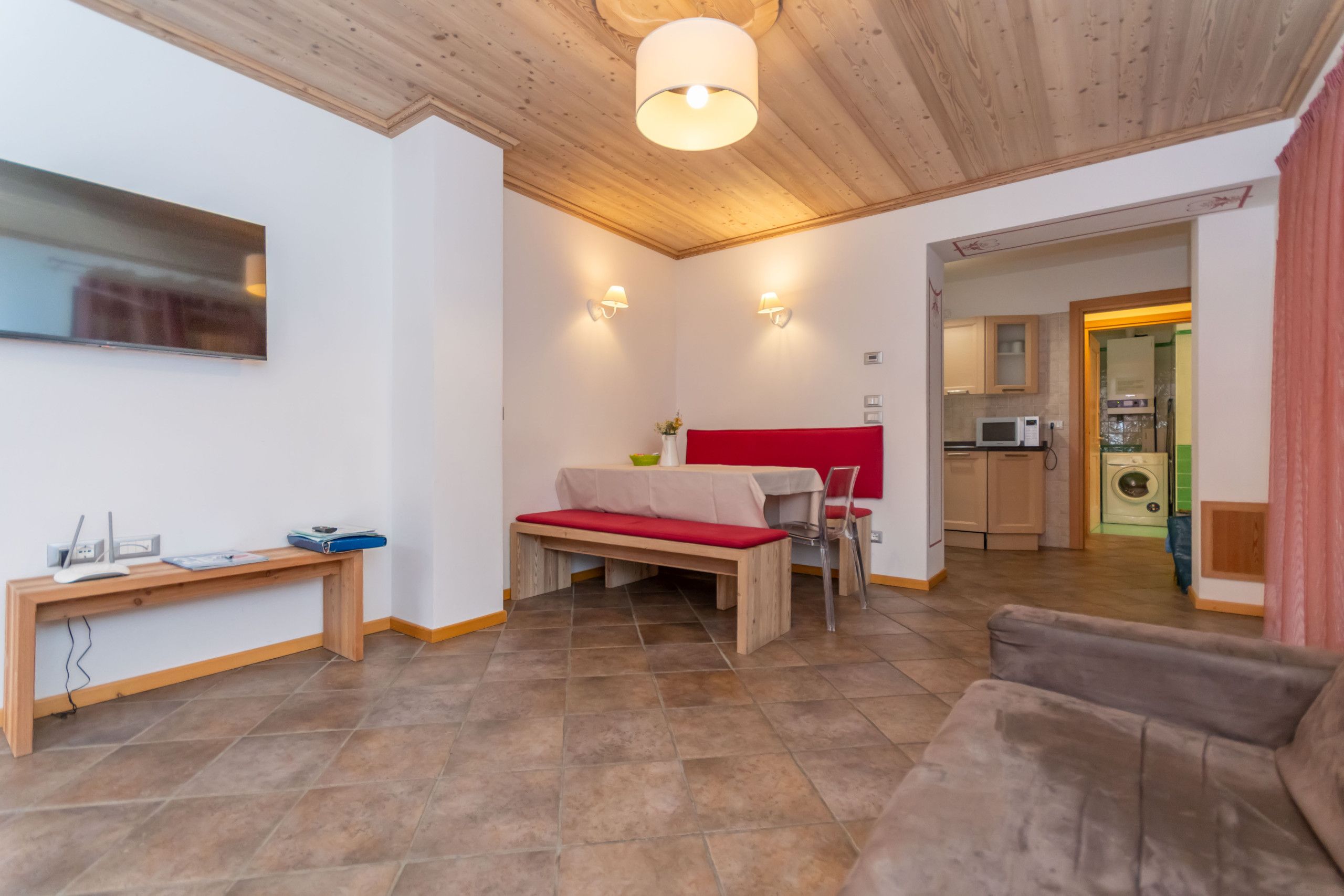 A modern living room with a wooden ceiling, a red sofa, a wooden bench, and a dining table.