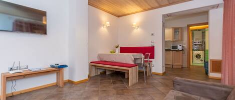 A modern living room with a wooden ceiling, a red sofa, a wooden bench, and a dining table.