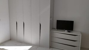 Una habitación con un armario blanco, un televisor sobre un soporte blanco y suelo de mármol.