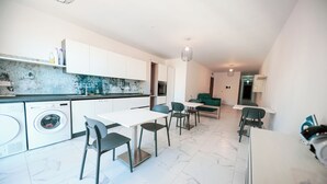 Una cocina moderna con lavadora integrada, un comedor con mesa y sillas, y un sofá verde al fondo.