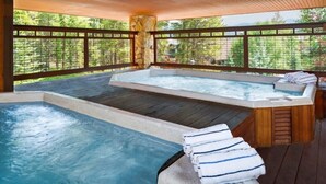 Un espace avec un bain à remous, une terrasse en bois, un pilier en pierre et une vue sur une forêt.