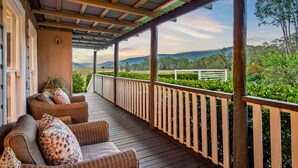 A covered porch with wicker furniture and a view of a landscaped garden and hills. - Prepare to Fall in Love (Millfield)