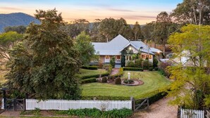 A two-story house with a well-maintained lawn, a white picket fence, and a garden with a fountain. - Prepare to Fall in Love (Millfield)