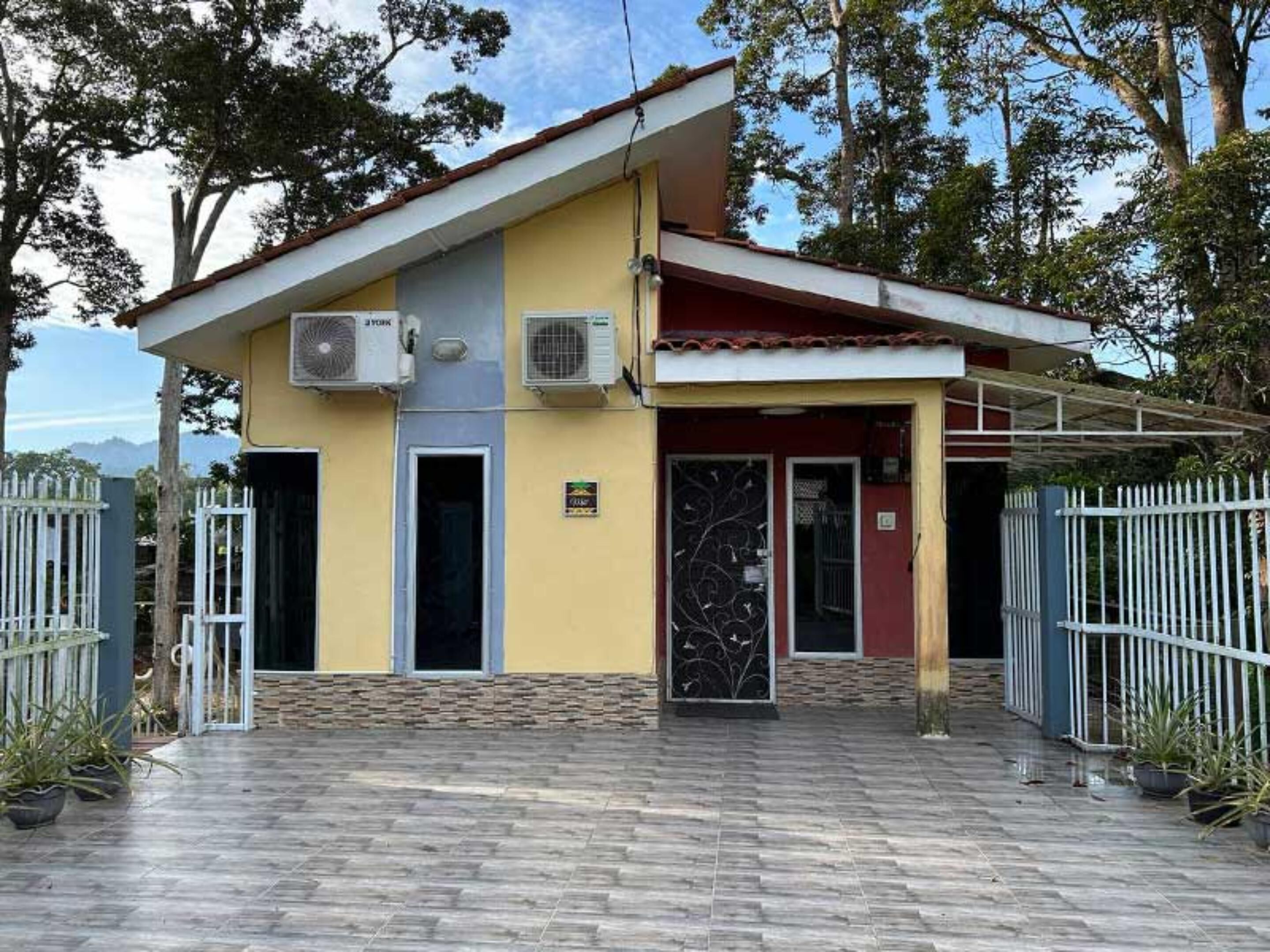 A two-story building with a flat roof, air conditioning units on the exterior, a gated entrance, and a paved driveway.