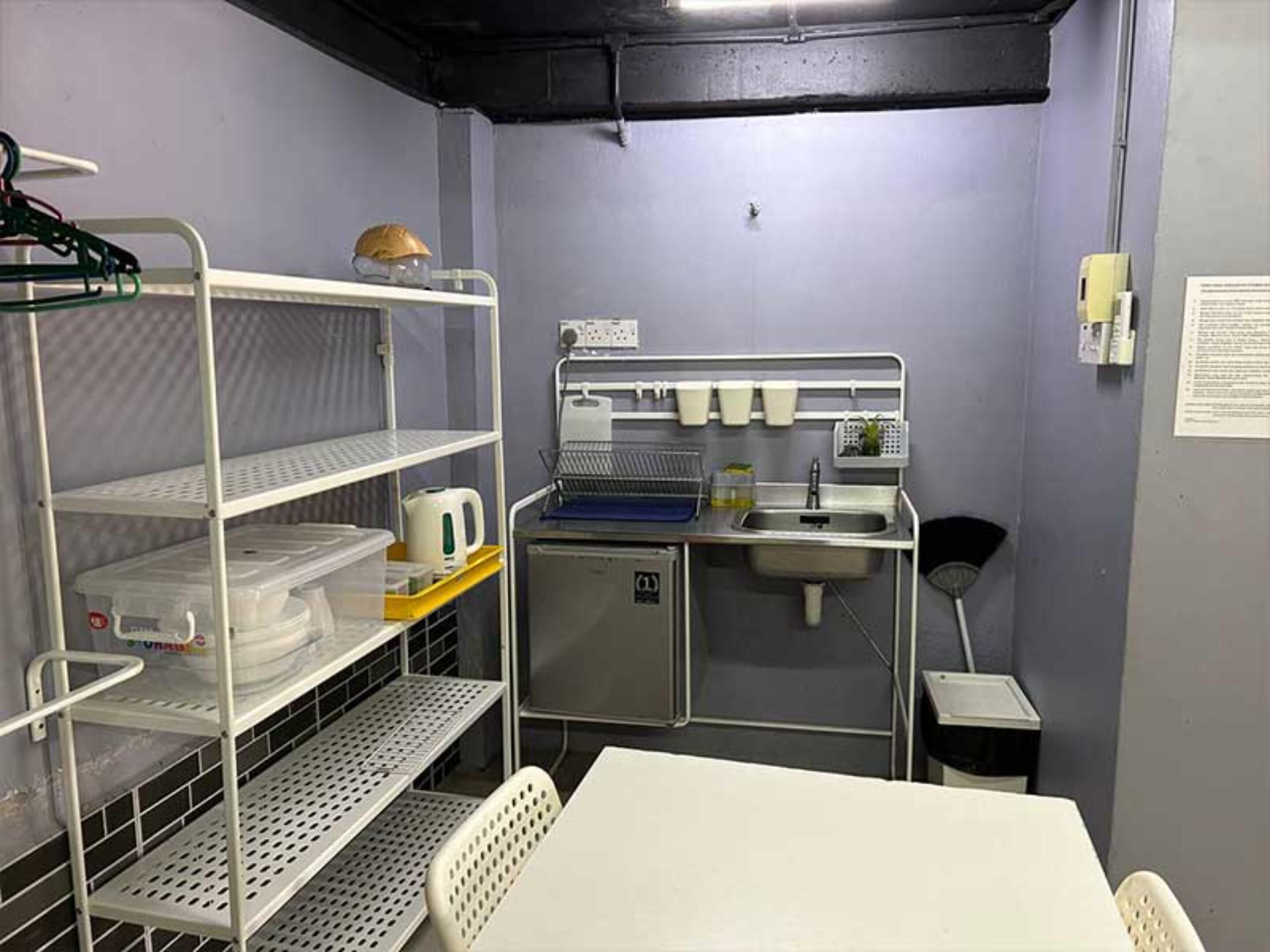 A compact kitchenette with a sink, a small refrigerator, and shelves with kitchenware.