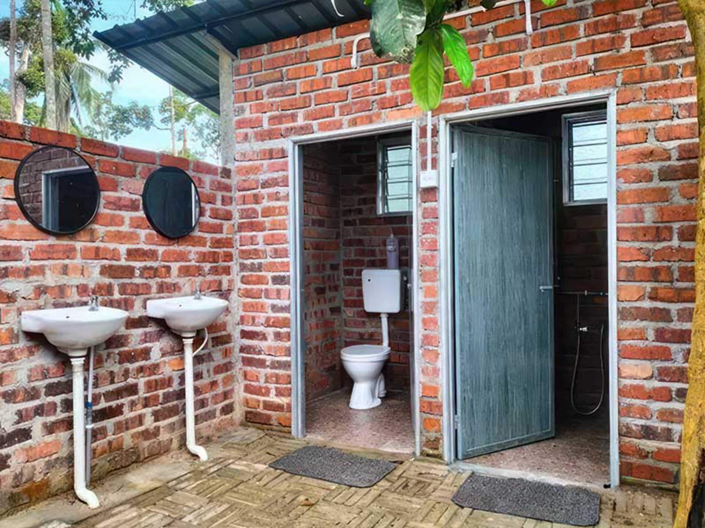 Une salle de bain rustique avec un mur en briques, deux lavabos, des toilettes et un espace douche.