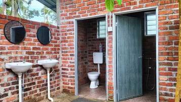 Une salle de bain rustique avec un mur en briques, deux lavabos, des toilettes et un espace douche.