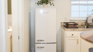 A compact kitchen with white cabinets, a white refrigerator, a small countertop, and a window with a plant above it. - The Laurelville in Hocking Hills Hills with Hot Tub (Laurelville)