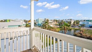 A balcony with a view of a residential area, including houses and a body of water. - Beachside Bliss l Golf Cart + Pool Table! (Port Aransas)