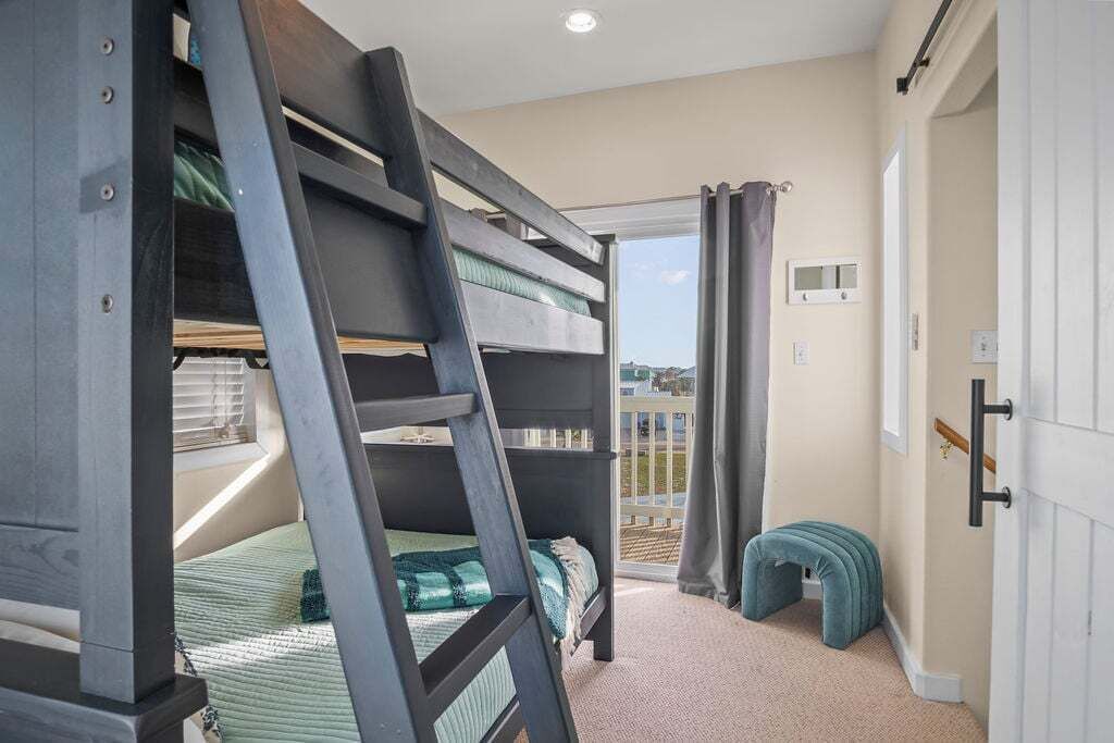 A bunk bed room with a ladder, a small stool, and a sliding glass door leading to a balcony.