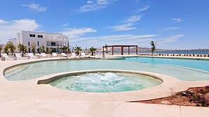 Una piscina con hidromasaje, sillas de descanso y un edificio con vistas al mar.