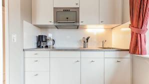A modern kitchen with white cabinets, a stainless steel range hood, a coffee maker, and a utensil holder.