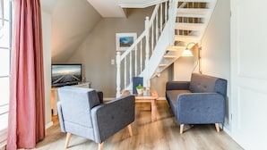 A modern living room with a staircase, a flat-screen TV, and two grey sofas.