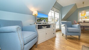 Un salon moderne avec un plafond haut, un plancher en bois et une grande fenêtre donnant sur l’extérieur.