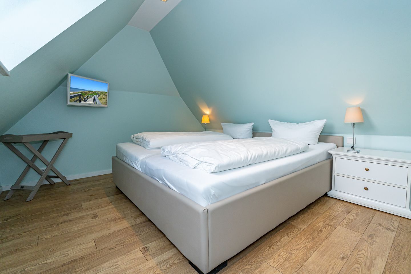 Ein Schlafzimmer mit einem Bett, Nachttischlampen, einem kleinen Tisch und einem Bild an der Wand.
