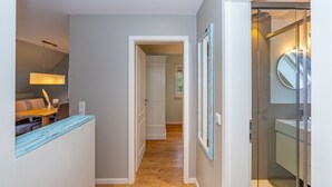 Un couloir avec un plancher en bois, un coin repas avec une table et des chaises, et une salle de bain dotée d’une cabine de douche en verre.
