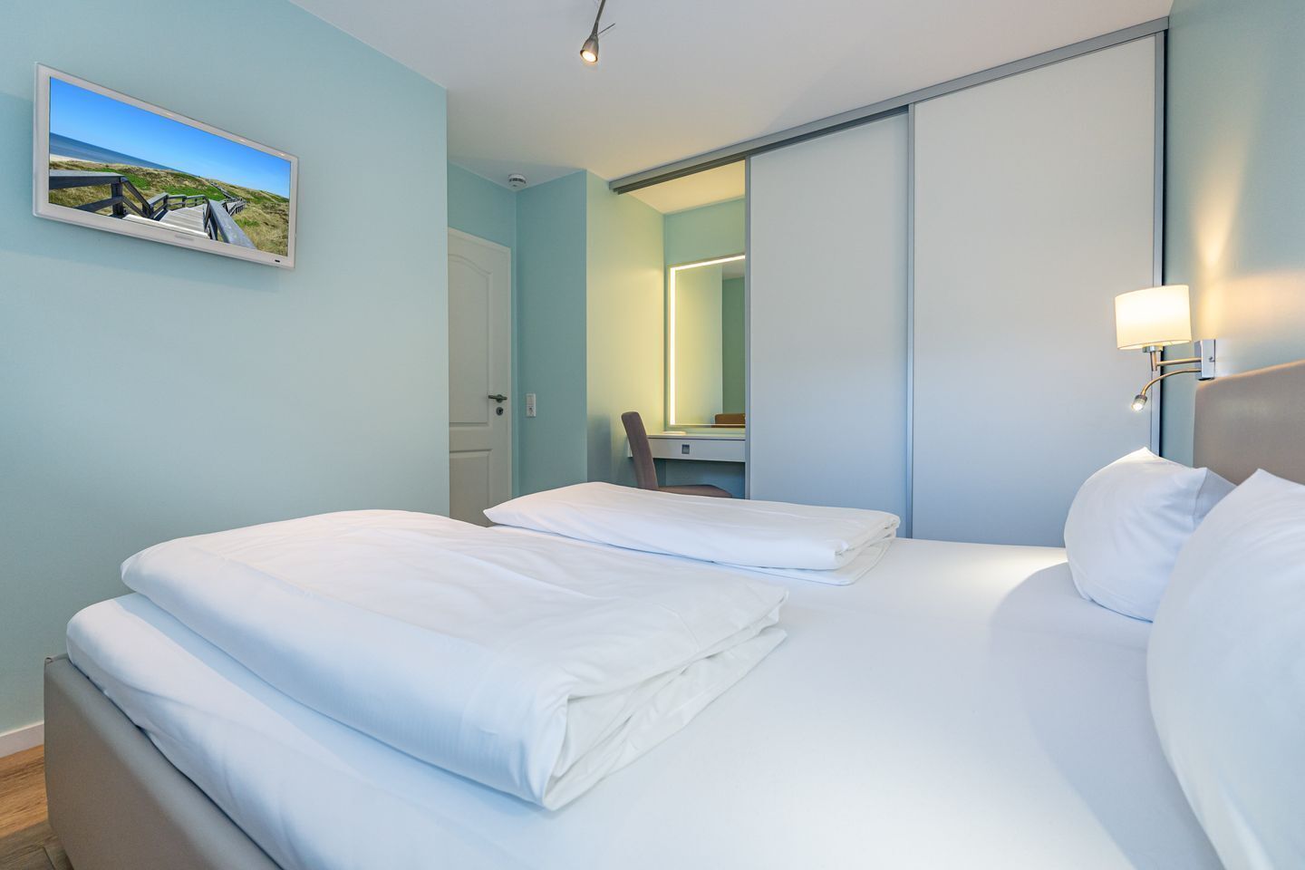 A hotel room with two beds, a large mirror, and a picture of a beach on the wall.
