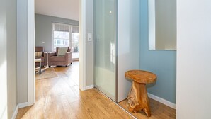 A hallway with a wooden floor, a glass door, and a small wooden stool. - Appartement Flut No. 5 - Appartement Flut 5 (Sylt)