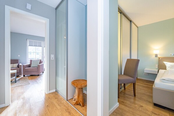 A modern hotel room with a wooden floor, a bed, a nightstand, and a chair.