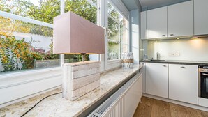 A modern kitchen with white cabinets, a marble countertop, and a large window overlooking a garden. - Appartement Flut No. 5 - Appartement Flut 5 (Sylt)
