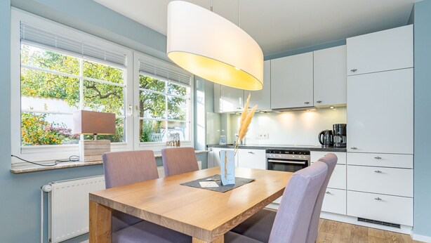 A modern kitchen with white cabinets, a wooden dining table, and a pendant light. - Appartement Flut No. 5 - Appartement Flut 5 (Sylt)