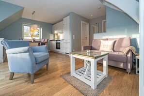 A modern living room with a glass coffee table, a blue armchair, and a pink sofa. - Appartement Ebbe No. 4 - Appartement Ebbe 4 (Sylt)