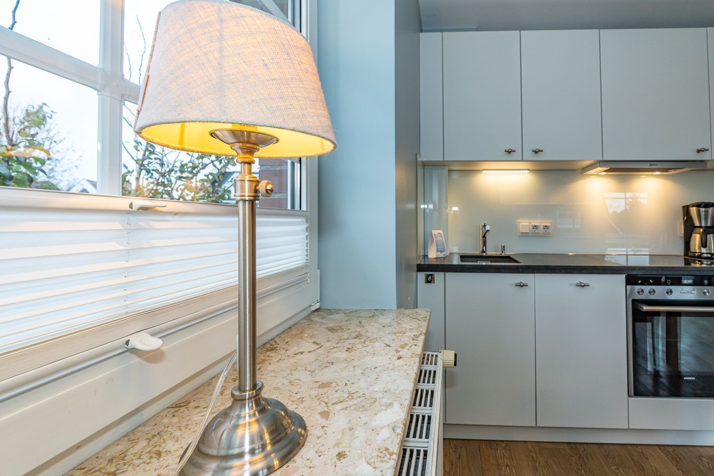 A modern kitchen with white cabinets, a built-in oven, and a window with blinds.