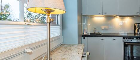 A modern kitchen with white cabinets, a built-in oven, and a window with blinds.