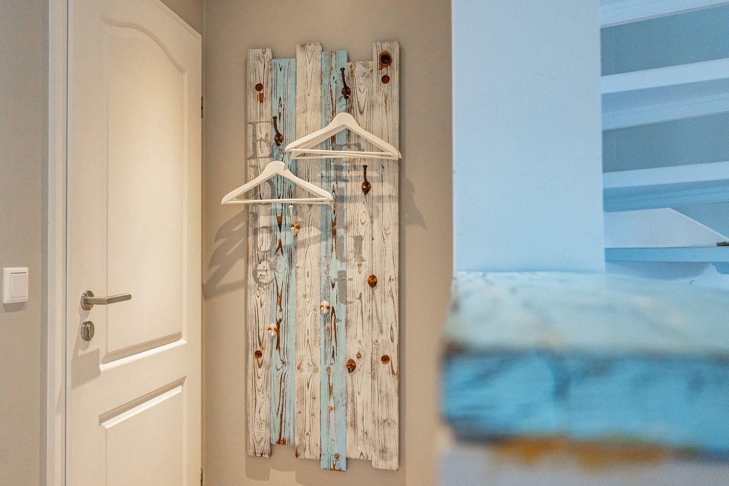 Un couloir avec une porte, un panneau en bois fixé au mur, doté d’un motif rustique, et un cintre blanc.