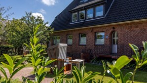 A brick house with a sloped roof, a small garden, and a patio area with a chair and table. - Appartement Hamburg, Deutschland (Westerland)